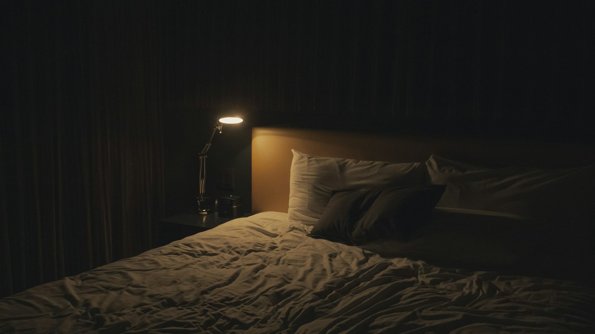 A warm table lamp glowing beside a bed