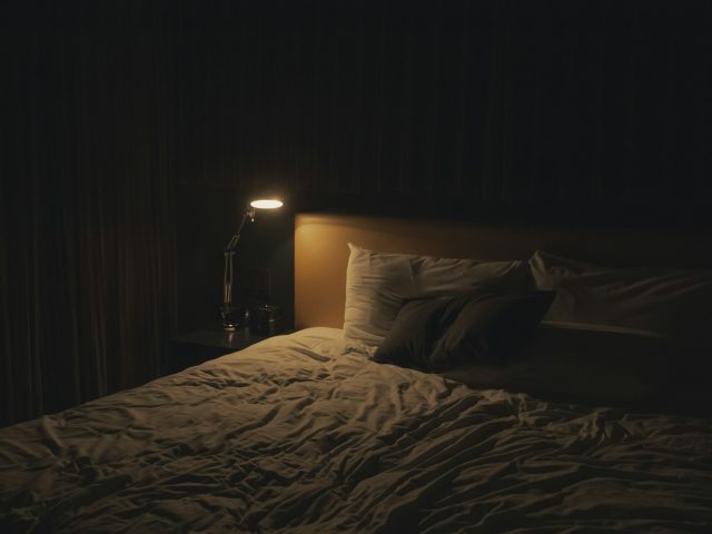A warm table lamp glowing beside a bed