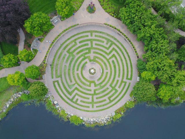 Aerial view of a circular hedge maze beside a lake