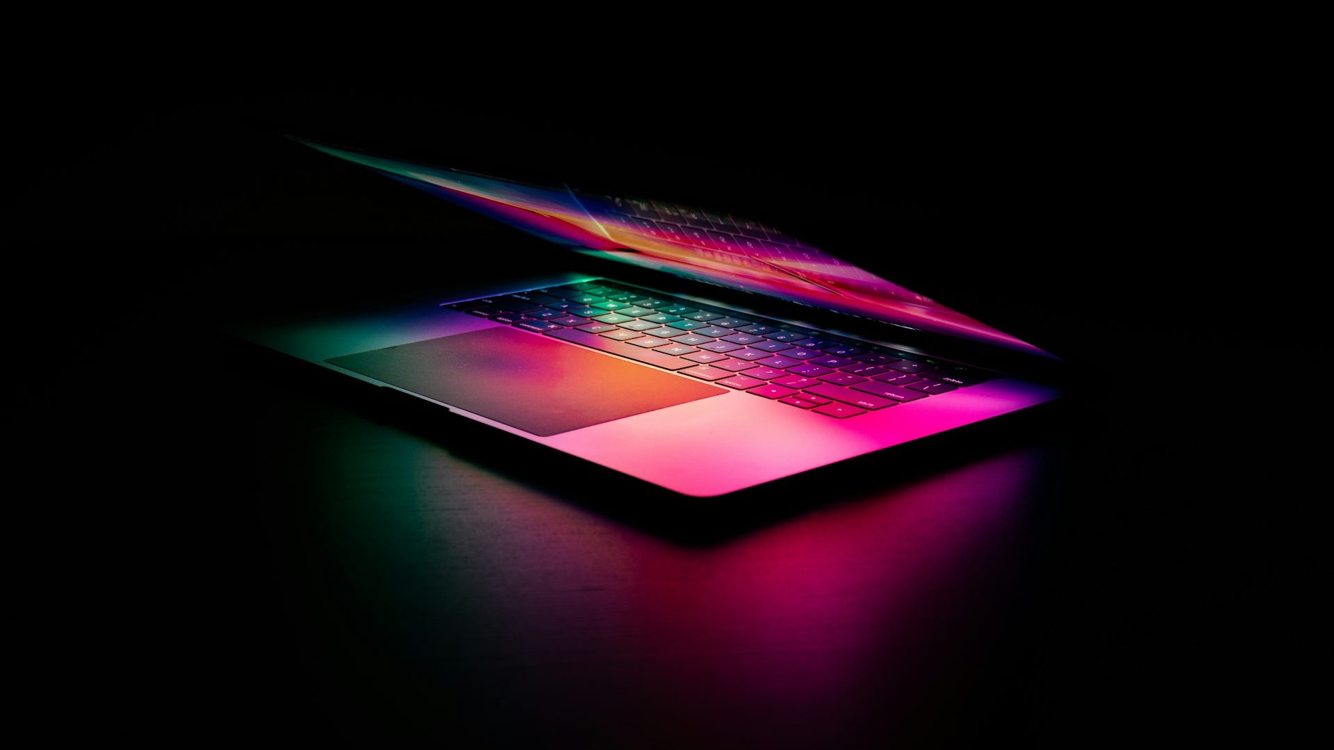A laptop keyboard glowing pink and green in a dark room